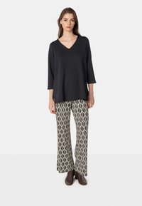 Svart V-ringad topp med 3/4-ärmar som kombineras med mönstrade vida byxor med en oval design i krem och brunt. Bruna ankle boots.
