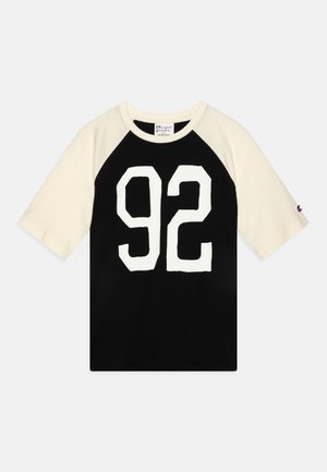 T-shirt noir avec des manches raglan crème courtes, affichant un grand numéro blanc "92" sur le devant. En coton avec un col rond.