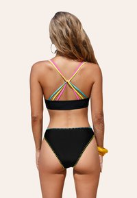 Bañador de dos piezas negro con un diseño entrelazado y tirantes multicolores. Costuras contrastantes notables en amarillo y azul.