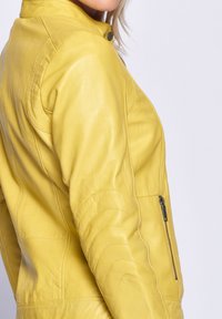 Gelbe Lederjacke mit taillierter Passform, glatter Textur und Reißverschlusstaschen. Verfügt über einen Stehkragen und gesteppte Akzente.