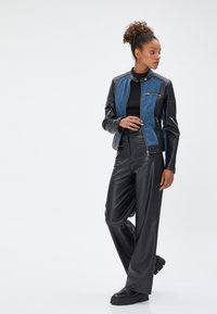 Schwarze Lederjacke mit vorderem Teil aus blauem Denim, taillierte Passform, Reißverschluss und gerippte Akzente. Kombiniert mit hochgeschnittenen schwarzen Lederimitat-Hosen.