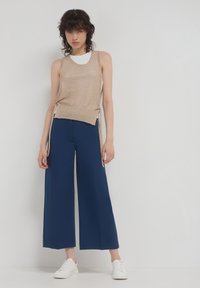 Top in maglia beige con scollatura a girocollo abbinato a pantaloni a gamba larga blu navy. Il modello indossa sneaker bianche. Design semplice e casual.