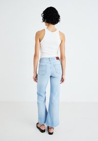 Ljusblå utsvängda jeans med hög midja, med en brun läderpatch och två bakfickor, som matchas med en vit linne.