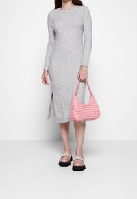 Donna che indossa un abito midi a costine grigio chiaro con spacco laterale, tiene in mano una borsa a tracolla intrecciata rosa e indossa mocassini beige con zeppa e fascette pastello.