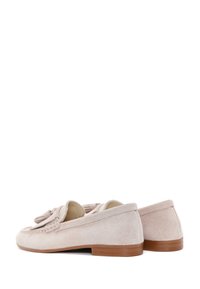 Mocasines de ante rosa pálido con puntera redonda, detalles de borlas y un tacón bajo de madera marrón. Textura suave y diseño sencillo.