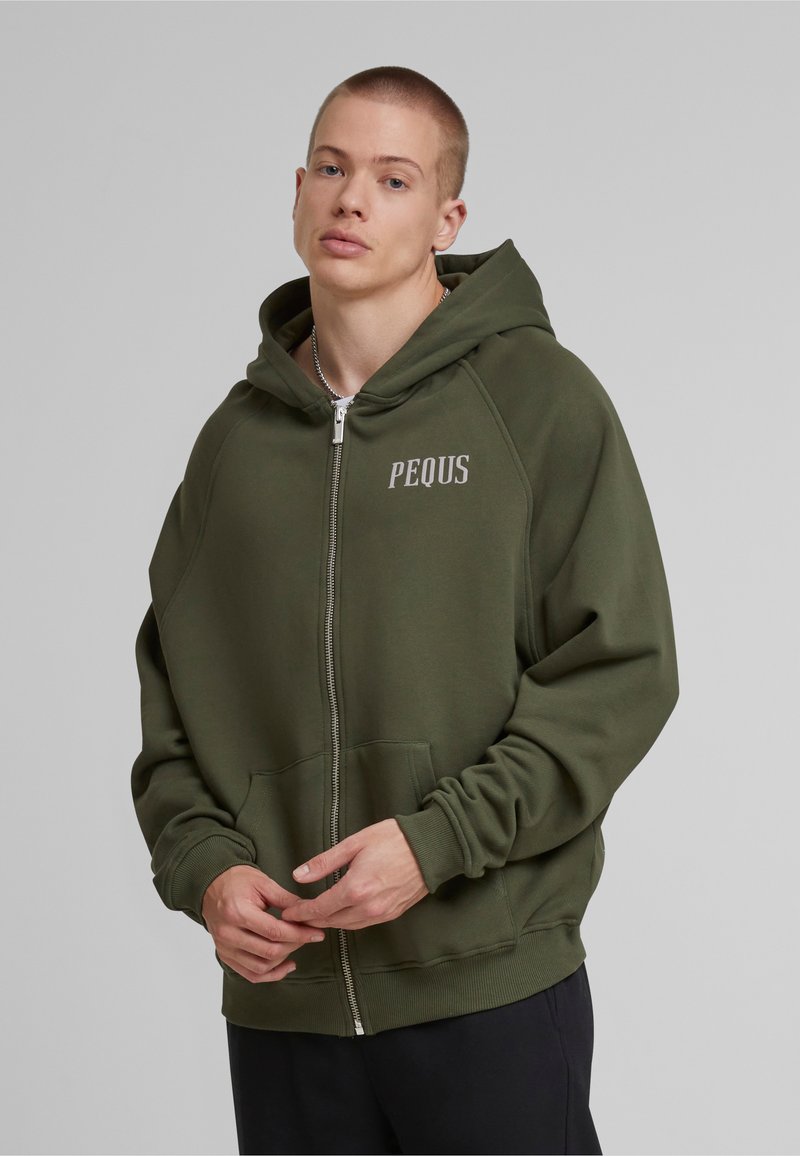 Sudadera verde con cremallera y grandes bolsillos frontales, puños y dobladillo acanalados. "PEQUS" impreso en gris claro en la zona izquierda del pecho. Textura de tela suave.