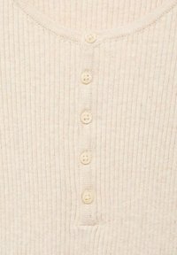 Haut henley crème à côtes avec sept boutons ronds de couleur claire sur le devant. Texture douce avec un col rond classique.