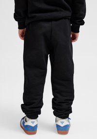 Schwarze Jogginghosen aus weichem Material, mit elastischen Bündchen an den Knöcheln und einer lässigen Passform, kombiniert mit blau-weißen Turnschuhen.