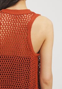 Ärmelloses Oberteil in Rostfarbe mit offenem Strickmuster, einem rundem Ausschnitt und strukturierter Oberfläche. Offener Rücken mit weiten Armausschnitten.