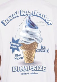 T-shirt blanc avec un motif d'un cône de glace à l'italienne avec des accents bleus, et du texte mettant en avant "vendeur de glace local" et "édition limitée."