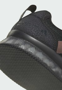 Czarne sportowe buty z teksturowaną cholewką, wzmocnionym piętą i teksturowaną gumową podeszwą z geometrycznym wzorem.