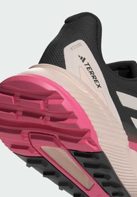 Zapatilla deportiva negra y rosa con parte superior texturizada, entresuela de espuma en contraste y suela de goma con patrón que muestra características de tracción.
