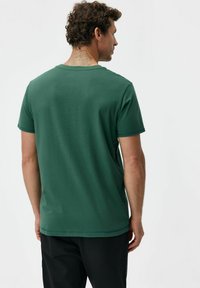 Zielona bawełniana koszulka z krótkimi rękawami, okrągłym dekoltem i gładką fakturą. Prosty wzór, bez wzorów ani widocznych elementów metalowych.