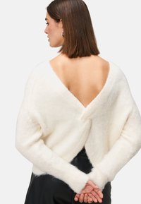 White, fluffy sweater with a deep V-back design. Features long sleeves with wide cuffs. Soft texture, minimalist style, and no visible fastenings.