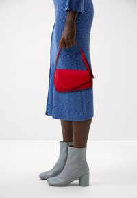 Rød læderhåndtaske med et bølgende design og kort rem, parret med en blå ribbet kjole og lysegrå lynlåse ankelstøvler.