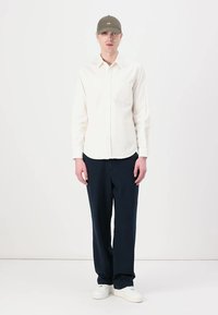 Light-colored button-up shirt, navy trousers, green cap, white sneakers. Simple design, relaxed fit, smooth texture, and minimal detailing.