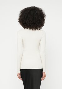 Λευκό μακρυμάνικο τοπ με ραβδώσεις, εφαρμοστή γραμμή και ψεύτικο λαιμό, σε συνδυασμό με μαύρη φούστα, εμφανιζόμενο από πίσω.