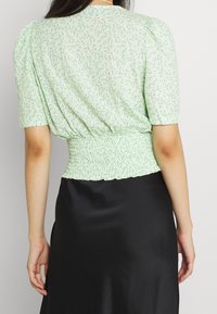 Blusa floreale verde con maniche a palloncino corte, vita smock e una texture morbida del tessuto. La vista posteriore mostra un colletto curvo.