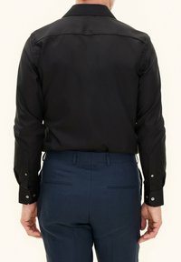 Zwart long-sleeve shirt met een standaard kraag, voorzien van knopenmanchetten. Gekocht met donkerblauwe broek, met een strakke en minimalistische uitstraling.