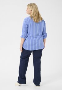 Hellblau gestreiftes Hemd mit aufgerollten Ärmeln, kombiniert mit dunkelblauen, weit geschnittenen Jeans. Glatte Textur mit lässigem Schnitt.