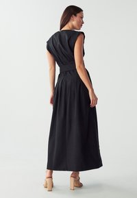 Abito maxi nero con maniche corte strutturate, vita cinte e gonna plissettata. Presenta una chiusura con zip sul retro e un tessuto liscio.