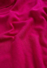 Tessuto di cotone fucsia con una texture morbida e liscia, caratterizzato da leggere pieghe che indicano la caduta e la flessibilità nel design.