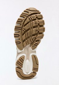 Podplat superge v bež in beli gumi. Ima teksturiran vzorec za oprijem, utore za prožnost in blagovno znamko na dnu.