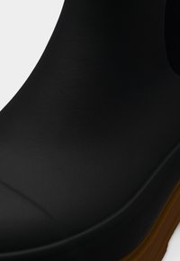 Μαύρη αδιάβροχη λαστιχένια μπότα με λεία επιφάνεια, στρογγυλεμένη μύτη και αντιθετική σόλα από ταμπά λάστιχο· χωρίς σχέδια ή πρόσθετες λεπτομέρειες.