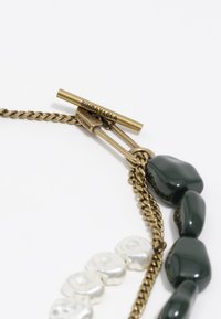 Collar de cadena dorada con acentos irregulares de piedra verde y cuentas parecidas a perlas blancas. Cierre marcado "BIMBA Y LOLA."