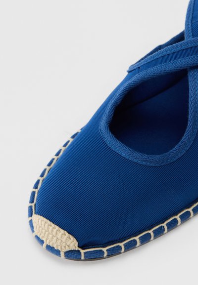 Plava platnena espadrila s zaobljenim prstima, pletenim jutenim naglaskom sprijeda i ukriženim trakama. Teksturirana površina, detalj sa šivenjem na rubu.