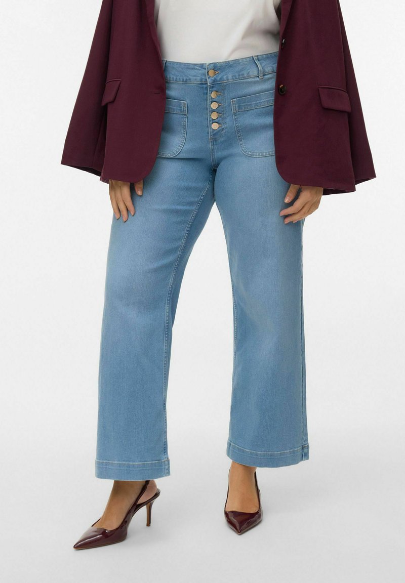 Jean bleu clair à jambes larges avec taille haute, doté de cinq boutons métalliques, poches avant et ourlet net. Associé à un blazer bordeaux et des talons.