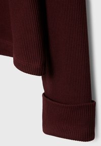 Gros plan sur une manche repliée et un poignet sur un pull en maille côtelée de couleur bordeaux foncé.