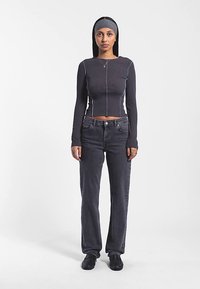 Figursydd långärmad topp i mörkgrå ribbad material med kontrasterande ljus sömnad. Kombinerad med högmidjade mörka jeans och svarta skor.