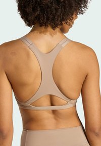 Sostén deportivo beige con diseño de espalda nadadora. Presenta tirantes estrechos y un detalle cortado en la parte posterior. Fabricado con un material suave y elástico.
