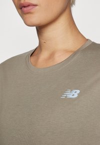 T-shirt à manches courtes vert olive avec un col rond et un logo New Balance bleu clair sur la poitrine gauche. Tissu lisse et léger.