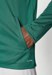 Πράσινο αθλητικό πουκάμισο με μακριά μανίκια διαθέτει πλαϊνή τσέπη, ομαλή υφή και το λογότυπο ClimaCool στο τελείωμα, σχεδιασμένο για άνεση και απόδοση.