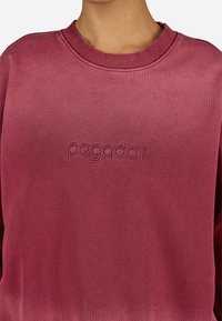 Bordový sveter s rebrovaným výstrihom do kruhu, na prednej strane s embosovaným logom "pegador". Jemná textúra a voľný strih.