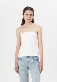 Hvit stroppeløs topp laget av ribbet stoff, med en rett utringning og dekorative knapper langs siden, parret med lyseblå jeans.