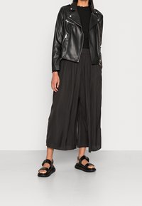 Sort læder bikerjakke over en sort ribbet top, parret med sorte vide bukser og sorte sandaler med en spænde detalje.