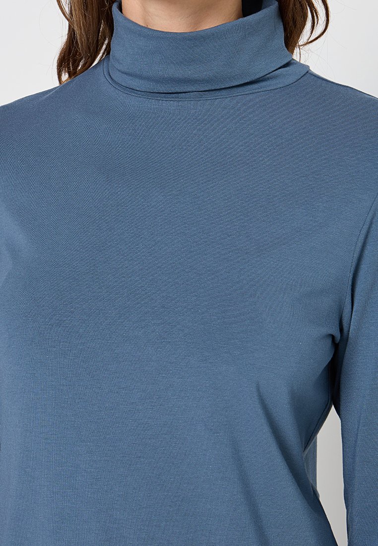Hellblaues Rollkragenoberteil aus weichem, dehnbarem Stoff, mit langen Ärmeln und einer glatten Textur sowie dezenten Details am Halsausschnitt.