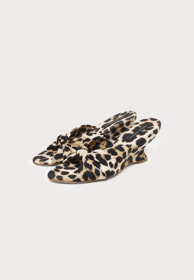 Paire de chaussures slip-on imprimé léopard avec petits talons compensés et détail noué sur le dessus, présentée sur un fond clair uni.