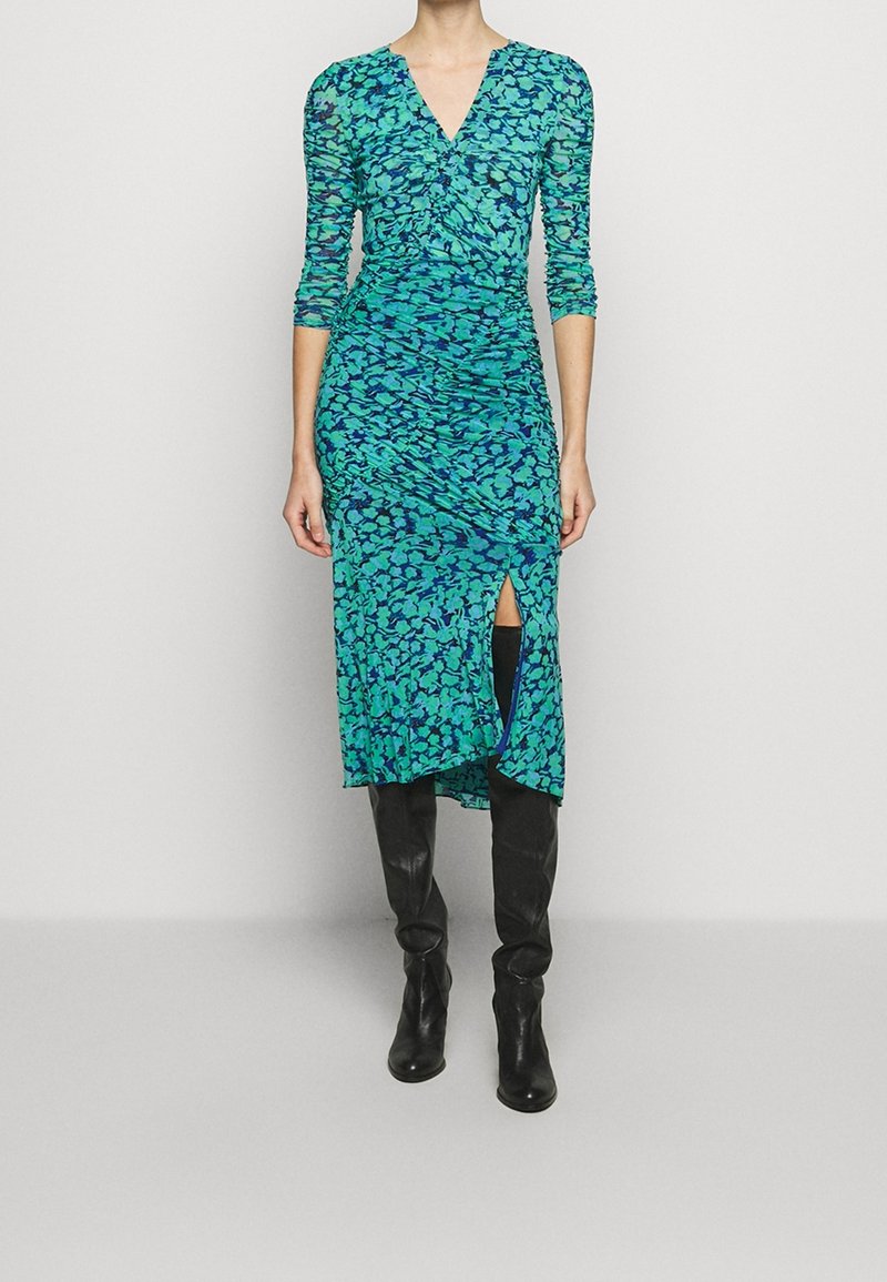 Femme portant une robe midi à fleurs bleu sarcelle et marine avec des manches trois-quarts et une fente devant, associée à des bottes en cuir noires montant jusqu'aux genoux.