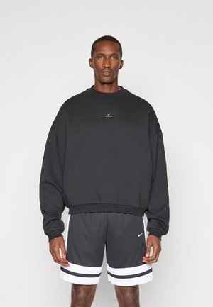 Sort oversized sweatshirt med rund halsudskæring og ribbede manchetter, parret med mørkegrå træningsshorts med hvide striber og logodetaljer.
