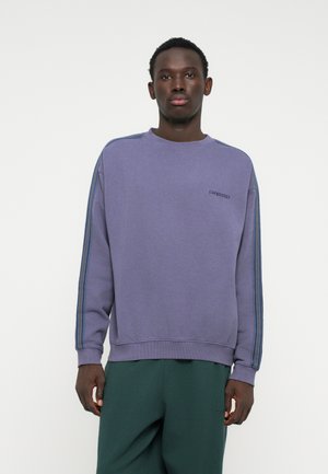 Felpa viola con scollo a girocollo, caratterizzata da strisce blu lungo le spalle. Tessuto morbido, vestibilità rilassata e logo ricamato sul petto.