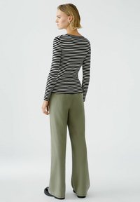 Haut à longues manches noir et blanc rayé associé à un pantalon large vert sauge. La tenue présente un torse ajusté et des jambes larges. Chaussures noires.