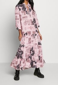 Růžové maxi šaty s dlouhým rukávem a stupňovitou spodní částí, s potiskem draka, textem a zavazováním na krku. Nosené s černými platformovými botami.