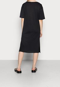 Svart, knälång t-shirtklänning i mjukt tyg; har korta ärmar, en avslappnad passform och sidoklipp för lättare rörelse.