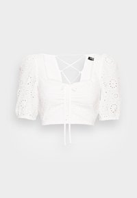 Top curto branco com mangas bufantes, tecido de ilhós com recortes florais, decote quadrado e detalhe de cordão nas costas. Textura suave.