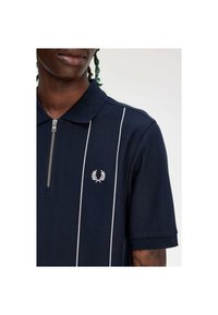 Navy poloshirt met een ritskraag, voorzien van witte verticale strepen en een klein geborduurd logo op de linkerborst. Gewoonde stof.