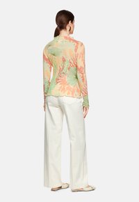 Langärmliges, leichtes Shirt mit einem cremefarbenen Grundton und bunten Blumen- und Blattmustern in Grün und Orange. Mit gewelltem Saum und taillierten Bündchen.